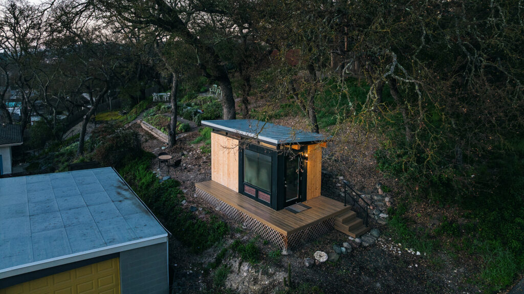 Modern prefab shed on hillside with deck and trees